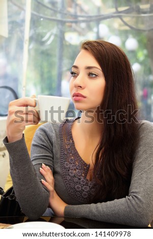 Young pensive woman drinking in a cozy cafe