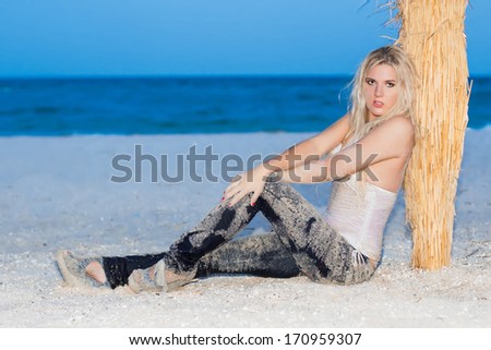 Pretty blond woman in wet clothes sitting near a palm