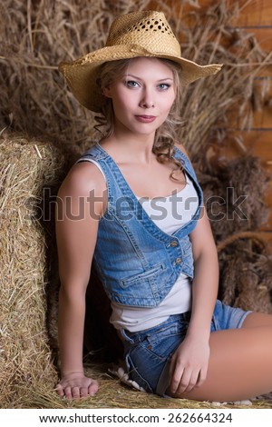 Sexy blond woman dressed in cowboy style posing on a haystack