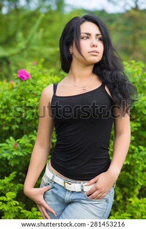 Attractive young woman in black t-shirt posing near the bushes