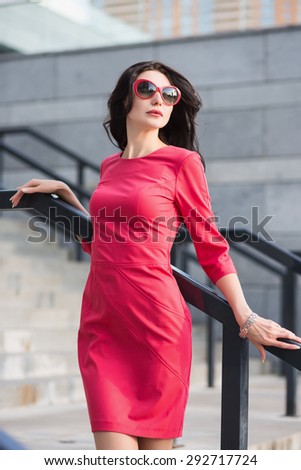 Sexy slim lady in red dress and sunglasses posing near the stairs outdoors