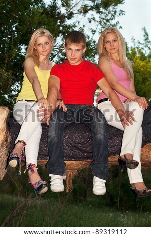 Two attractive blonde and young man sitting on a tree branch