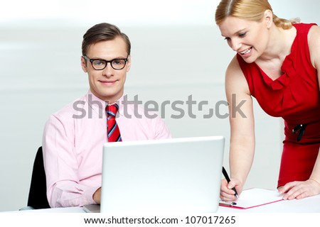 Woman writing information from laptop while businessman looking at camera