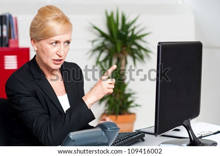 Angry woman in office indicating at computer led screen