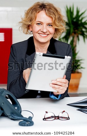 Cheerful businesswoman using portable device and looking at camera