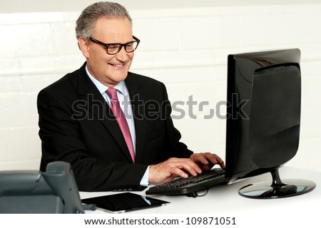 Casual businessman working in office sitting at desk typing on keyboard looking at computer screen