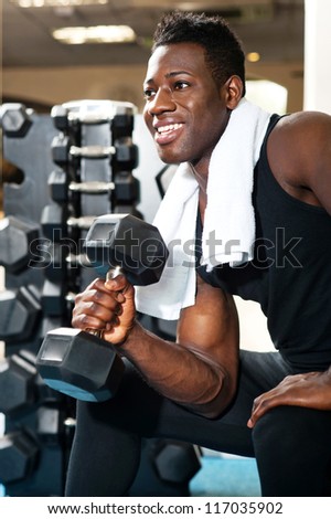 Young gym instructor toning his biceps, triceps and forearm while exercising with heavy dumbbell