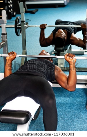 An african male bodybuilder trying to lift the barbell. Reflection can be seen in the mirror