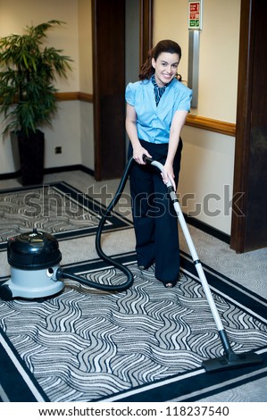 Staff cleaning carpet with a vacuum cleaner. Smiling and enjoying her work