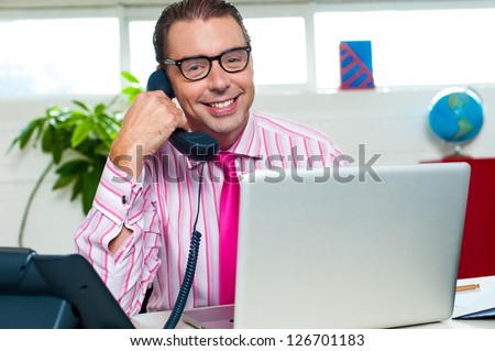 Smiling male representative engaged over a business call with laptop in front of him.
