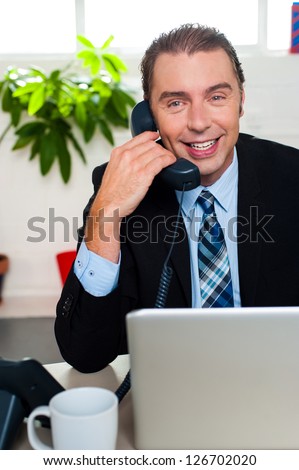 Executive in office talking over the phone, happy face.