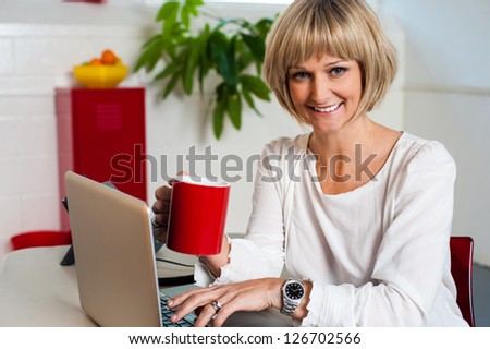 Corporate lady holding coffee mug and working on laptop. Indoor office shot.