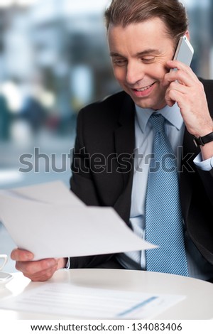 Positive corporate guy communicating on phone with reports in hand.