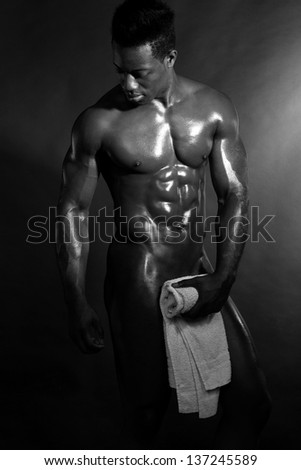 Wet muscular man wiping himself with a towel, dark background.