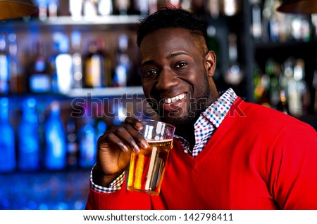 Smiling young african guy enjoying fresh beer at pub.
