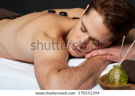 Relaxing young guy with hot stones on his back