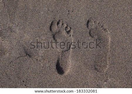 Two footprints in the sand, near the beach