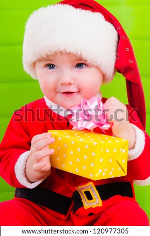 cute kid in Santa Claus clothes. sitting on a green chair and holding a big gift box