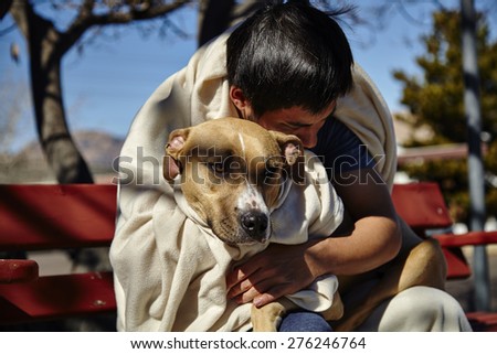 Man with dog wrapped in blanket sitting on bench bent over dog