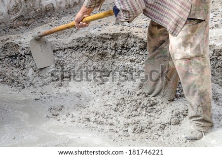 Construction worker with a hoe and a concrete mixer making cement, Construction worker mixing cement