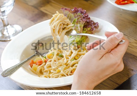 Spaghetti noodles with cream sauce on white plate, swirl of spaghetti on a fork