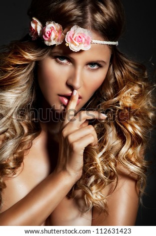 Sensual, natural  blond woman with flower on her head and long shiny, curly blond hair . Studio