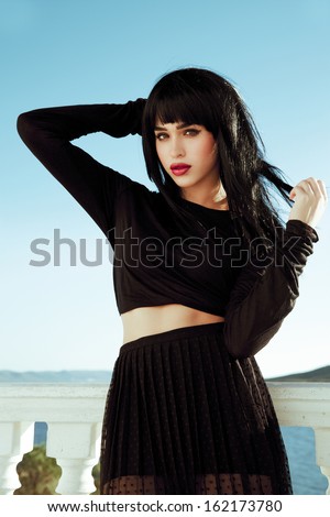 Vogue style brunette in Asian style by the sea. Fashion art. Woman with long black hair and black outfits. Blue sky backgrounds. Bright make up face .Red lips . sexy look. Street style. Vertical shot.