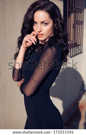 Beautiful woman with long black wavy hair and black outfits. Bright make up face .Sexy look. Street style. Vertical shot.