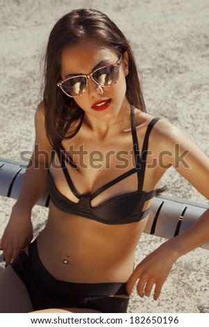 Attractive tanned woman in black bikini posing on hot sunny day. Bronze tan. outdoors shot. vertical