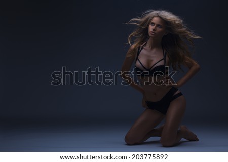 Tanned summer woman in glamorous bikini and long curly hair. fool body shot. toned in warm colors. studio shot on a dark blue background. horizontal. copy space for your text