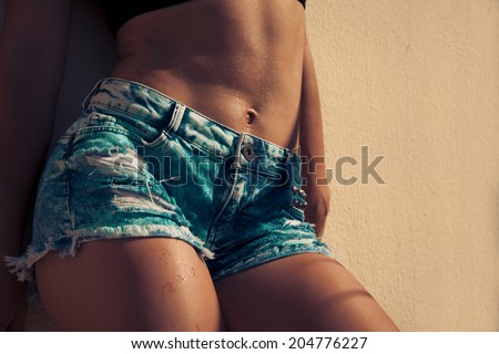 Beautiful woman body in denim jeans shorts . Toned in warm colors.