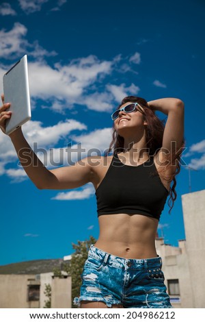 Beautiful, smiling woman take a picture of herself with a tablet. Selfie style. Toned in warm colors. Copy space for your text. Outdoors shot, vertical.