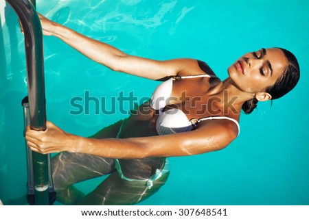 young brunette woman in the swimming pool. Tanned beauty. Outdoors shot. Horizontal