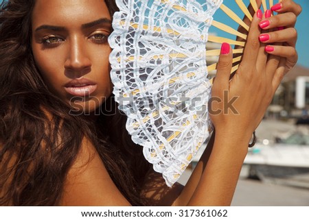 Luxury fashion style portrait of Latin woman with fan. Manicure nails . Cosmetics and make-up . Toned in warm colors. Horizontal shot.