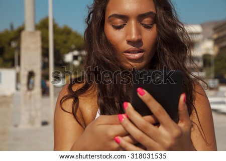 Smiling young female reading message on her smart phone. Shot on a sunny day. Lifestyle and technology concept. Horizontal shot, outdoors