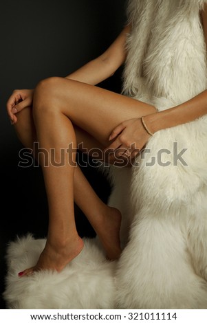 Long woman legs isolated on white fur coat . Luxury jewelry and white fur. Studio shot.Vertical photography