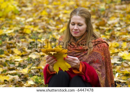 Thoughtful woman sitting in maple leaves holding some of them in her hands and smiling
