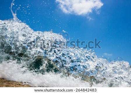 wave hitting the beach with a bright blue sky in the background