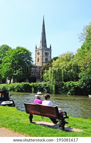 STRATFORD-UPON-AVON, UK - MAY 18, 2014 - Holy Trinity Church seen across the River Avon with a couple sitting on a bench in the foreground, Stratford-Upon-Avon, Warwickshire, UK, May 18, 2014.