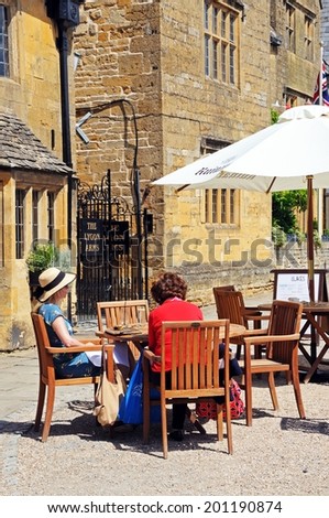 BROADWAY, UNITED KINGDOM - JUNE 12, 2014 - Two women sitting at a pavement cafe by the Lygon Arms Hotel along High Street, Broadway, Cotswolds, Worcestershire, England, UK, Europe, June 12, 2014.