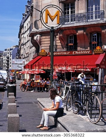 PARIS, FRANCE - JULY 18, 1996 - Young woman sitting by a Metro sign with a pavement cafe to the rear in the city centre, Paris, France, Western Europe, July 18, 1996.