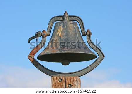 An old bell on a post next to a church and grade school.
