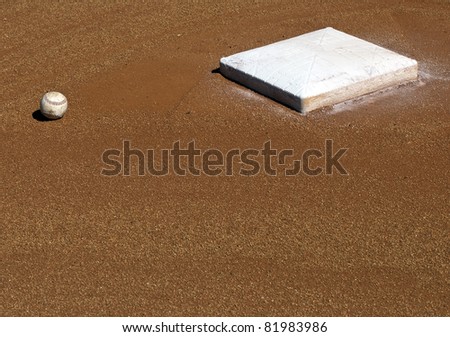 The 2nd base of a baseball diamond with a baseball lying nearby.