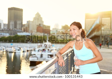 Woman city runner resting after running workout. Female fitness model smiling happy drinking water enjoying a break. Beautiful fit mixed race Asian Chinese and Caucasian woman outdoors.