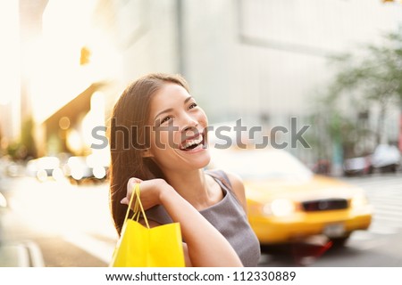 Shopper woman on Manhattan, New York City shopping having fun laughing outside in streets of New York. Fresh blissful mixed race Asian / Caucasian girl holding shopping bag.