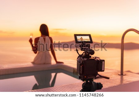 Video camera filming actress woman acting for movie on luxury hotel location behind the scenes of shoot. Professional videography equipment shooting outdoor at sunset.