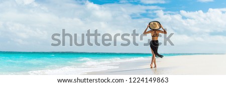 Luxury travel summer beach vacation woman walking in black beachwear skirt and hat on paradise white sand Caribbean beach. Lady tourist on Caribbean holiday vacation resort. Banner panorama landscape.