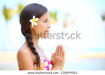 Serene meditation - meditating woman on beach smiling happy in profile on hawaiian beach. Beautiful portrait of mixed race Asian / Caucasian female model relaxing on Hawaii.