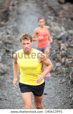 Runner man running on trail in cross-country run outdoors training on Hawaii, Big Island for marathon or triathlon. Fit young fitness model man and Asian woman in background training together outside.