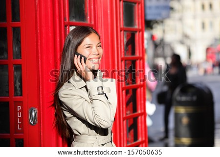 London business woman on smart phone by red phone booth. Communication concept with young multiracial Asian businesswoman on smartphone or mobile phone in London, England, United Kingdom.